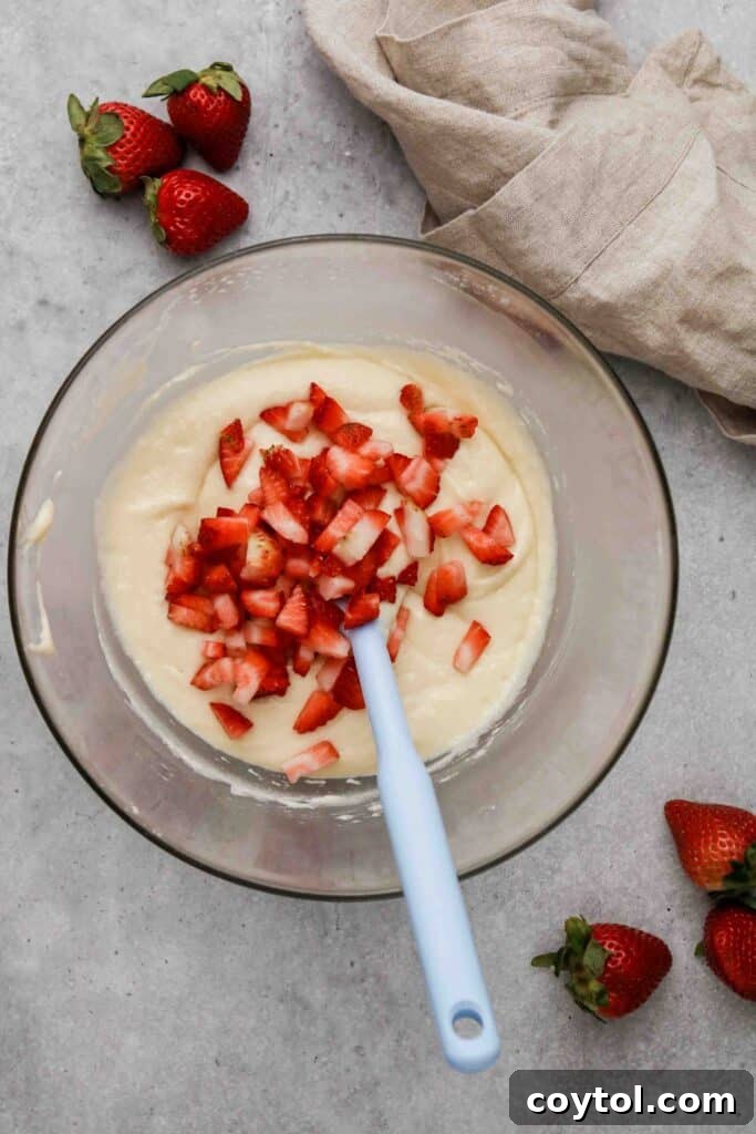 Freshly chopped strawberries being gently folded into the prepared muffin batter.
