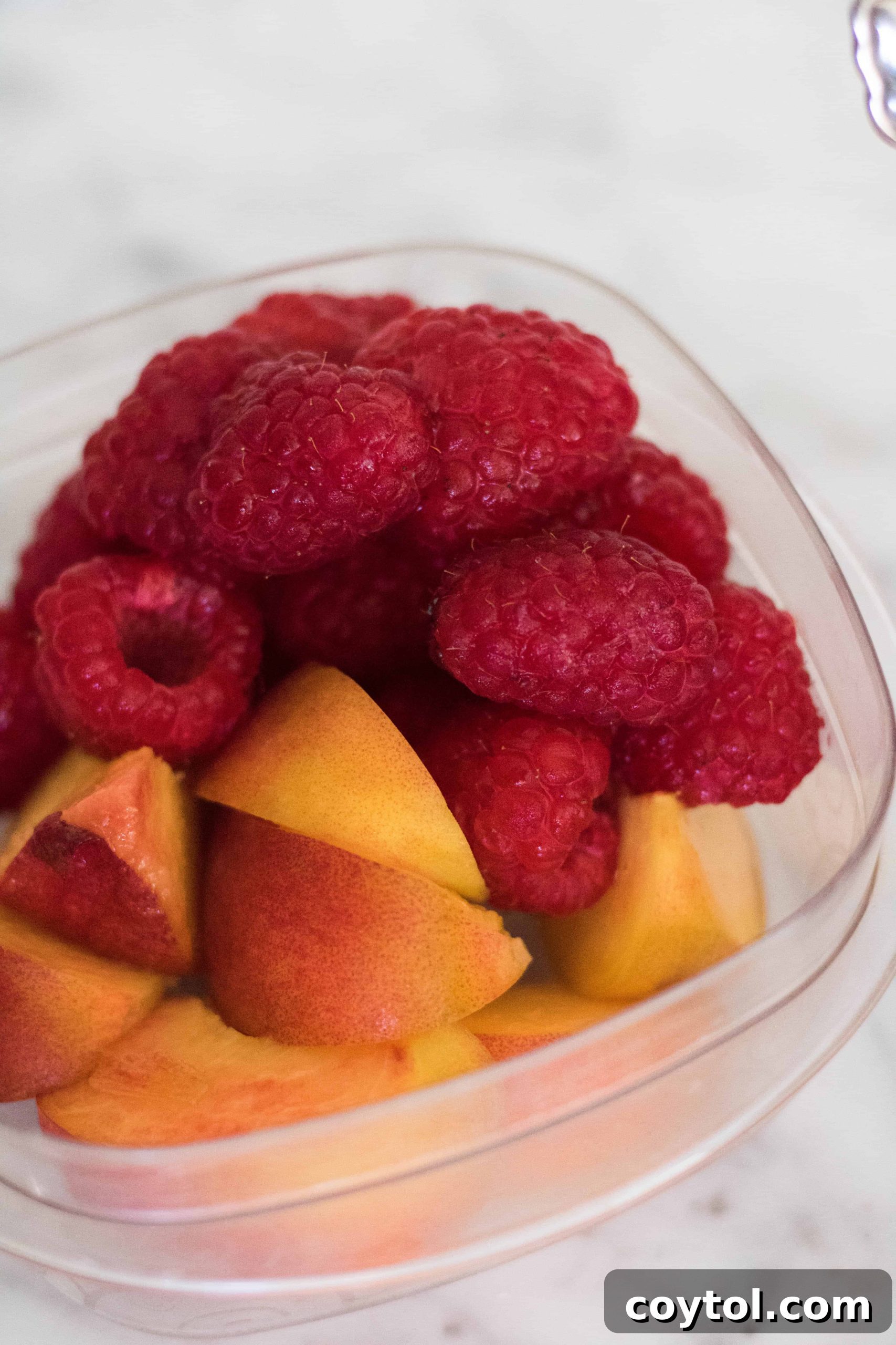 A side serving of fresh, ripe raspberries and peaches, perfect for a healthy dessert or snack.