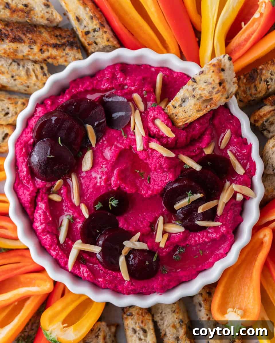 Beet hummus served in a bowl with crostini and fresh vegetables