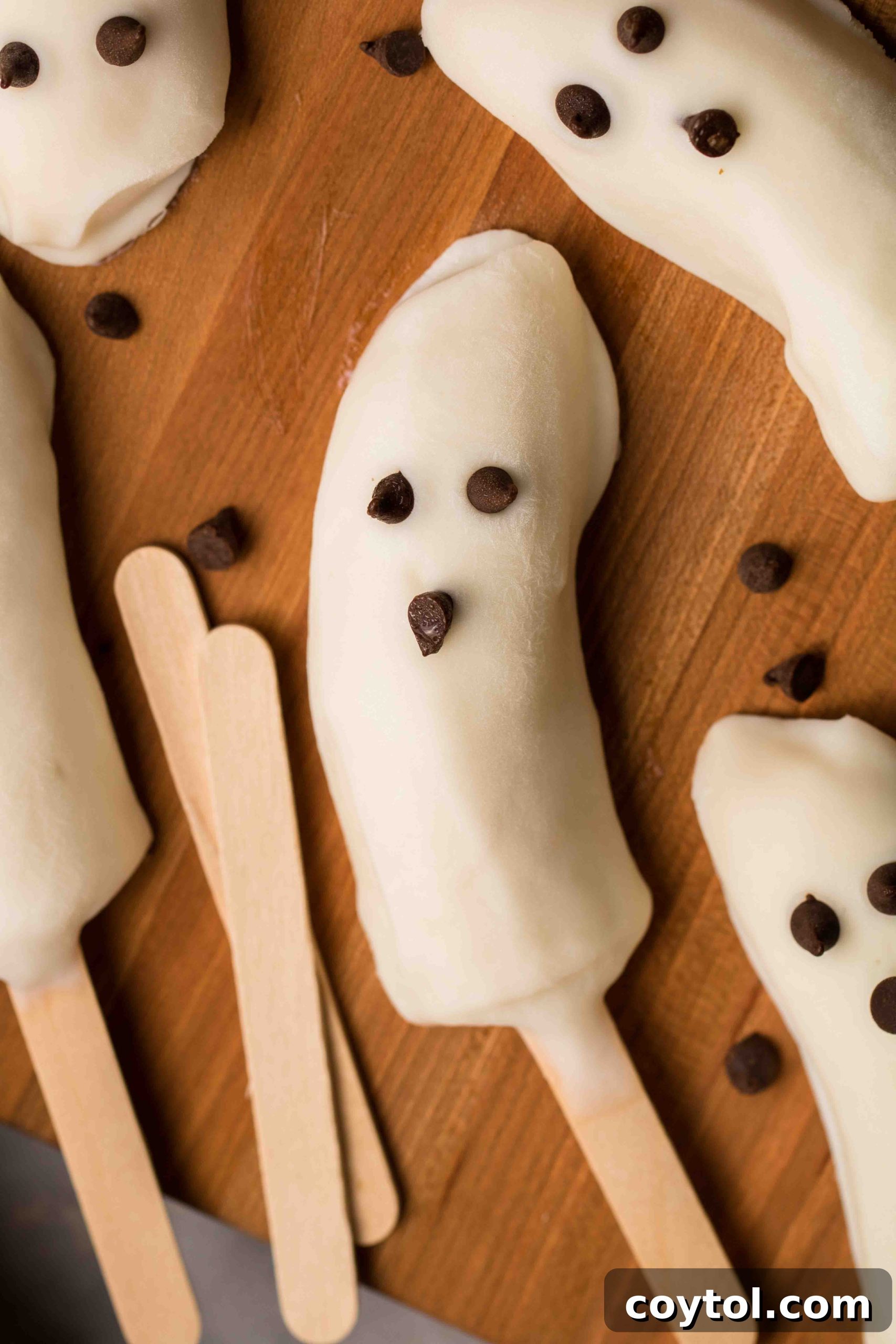 Delicious and healthy Halloween frozen banana ghosts covered in vanilla yogurt with chocolate chip eyes and mouth, perfect for a spooky treat.