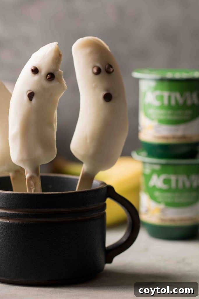 Close-up of a Boonana, a frozen banana ghost, showing the creamy vanilla yogurt coating and mini chocolate chip eyes and mouth.