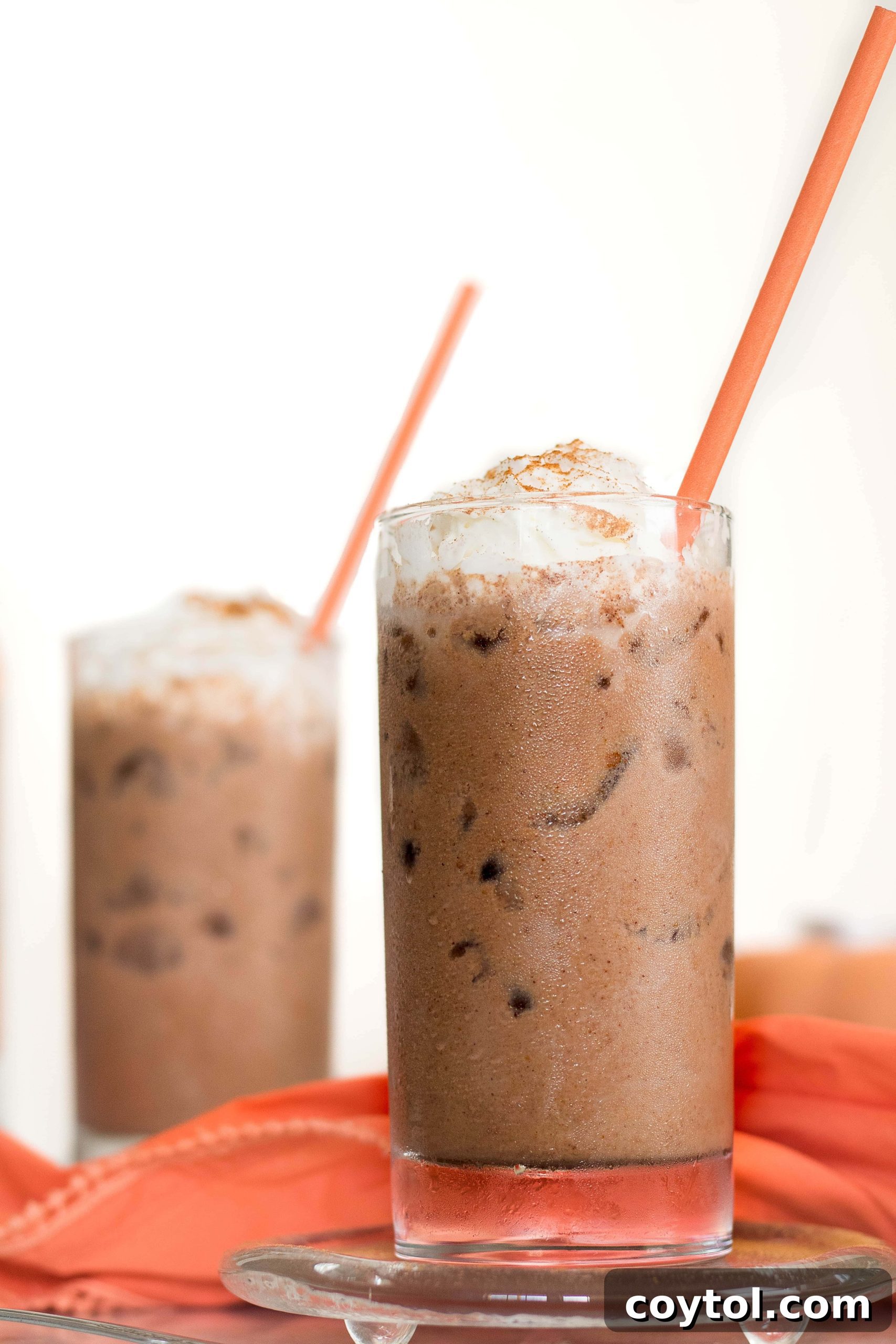 Cool and refreshing Iced Vegan Pumpkin Spice Hot Chocolate in a tall glass, garnished with vegan whipped cream and a sprinkle of cinnamon, perfect for satisfying fall cravings on a warm day.