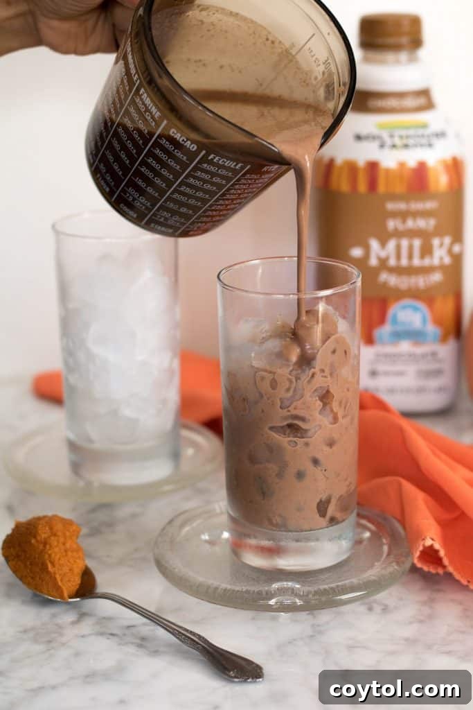 Close-up of a glass of Iced Vegan Pumpkin Spice Hot Chocolate, showing its rich, creamy texture topped with a delicate layer of foam and a hint of spice.