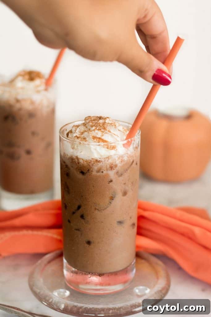 Two glasses of Iced Vegan Pumpkin Spice Hot Chocolate, elegantly garnished with generous swirls of vegan whipped cream and a dusting of spice, ready for a delightful autumn indulgence.