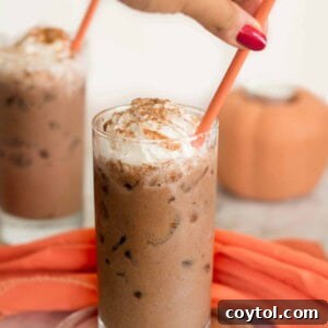 A refreshing glass of Iced Vegan Pumpkin Spice Hot Chocolate, topped with creamy vegan whipped cream and a sprinkle of pumpkin pie spice.