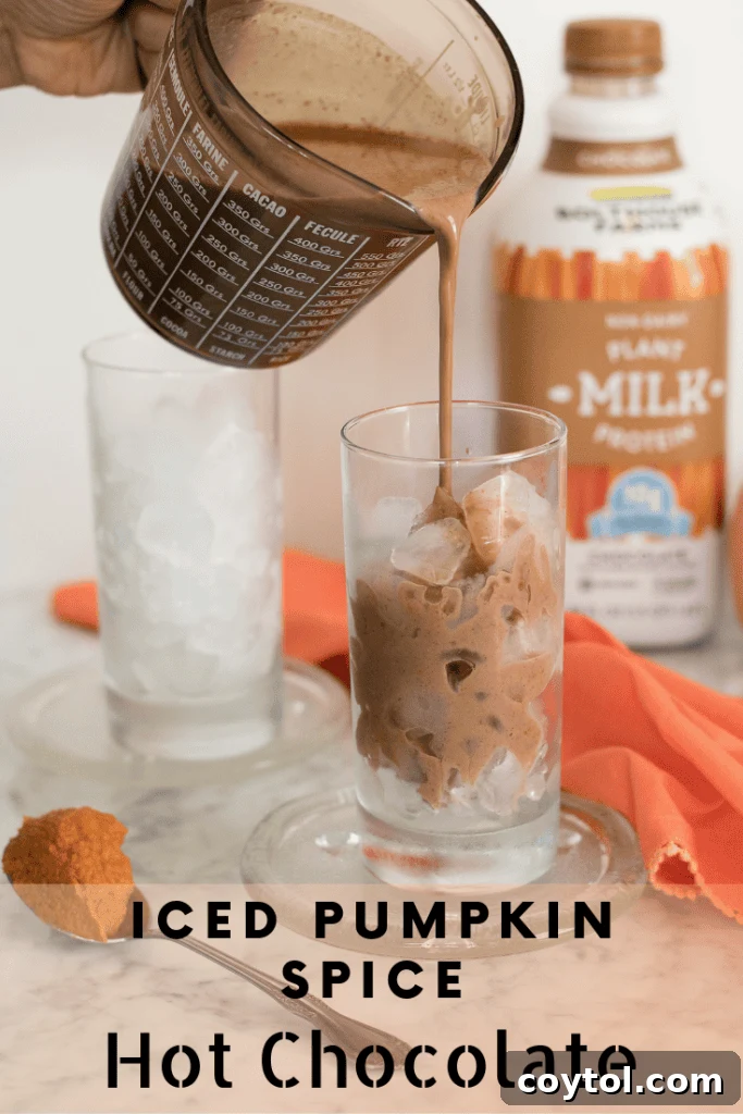 Iced Vegan Pumpkin Spice Hot Chocolate in a stylish glass, garnished with vegan whipped cream and a delicate sprinkle of spice, perfect for a modern fall aesthetic.