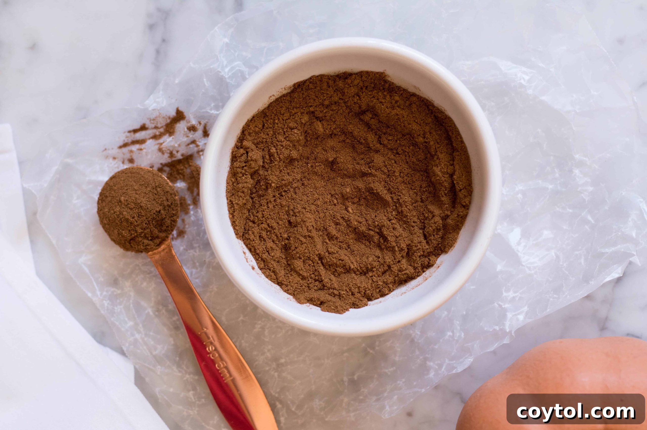 A small glass jar filled with homemade pumpkin pie spice, with a wooden spoon resting beside it, on a rustic background.