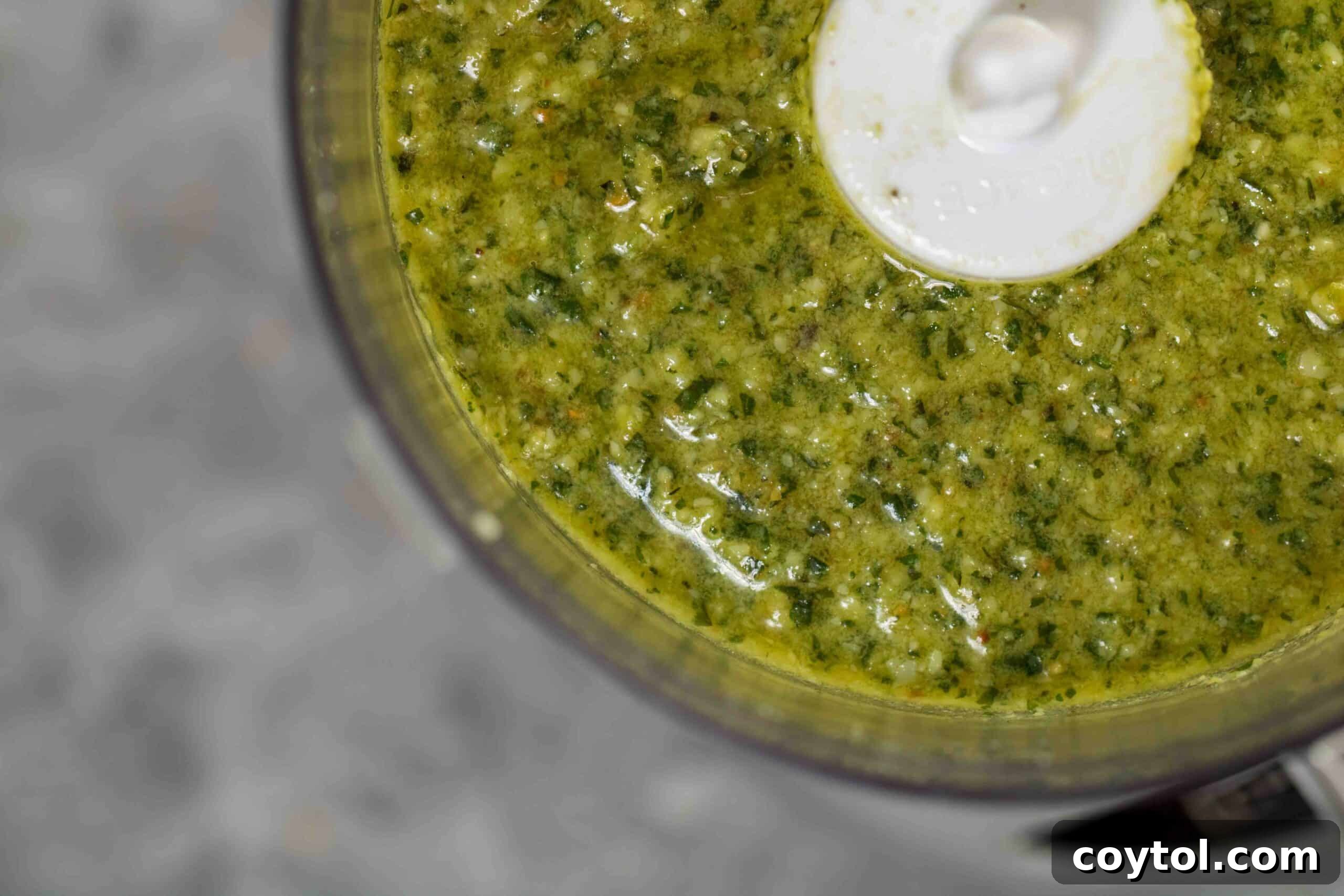 Close-up overhead shot of the rich, textured green surface of freshly made pesto, highlighting its vibrant color and consistency.