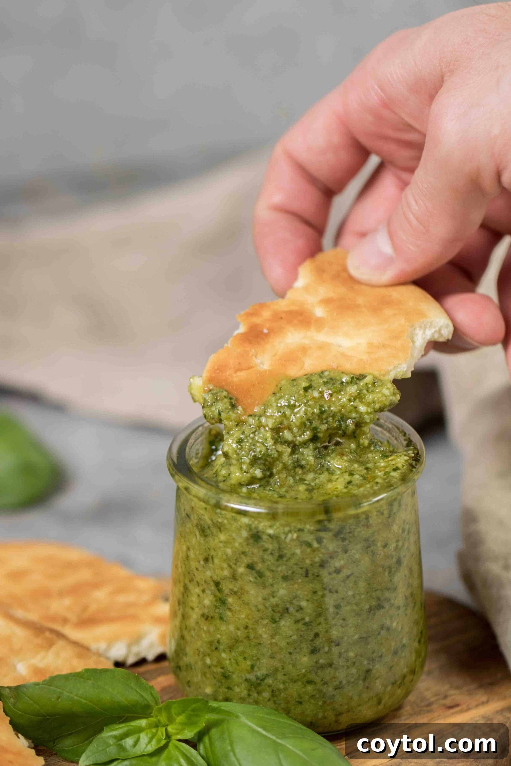 Crusty flatbread pieces dipped into a bowl of vibrant homemade pesto sauce, with fresh basil leaves scattered around.