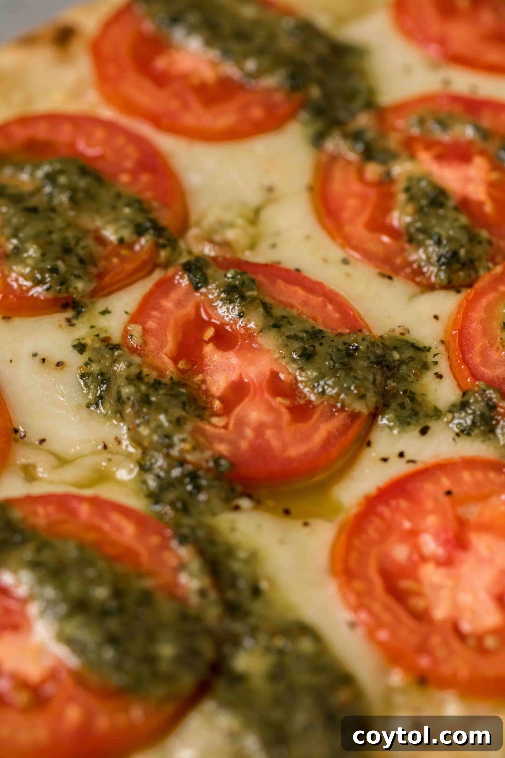 Close-up view of a slice of pesto margherita flatbread pizza showcasing melted mozzarella, vibrant red tomato slices, and fresh green pesto.