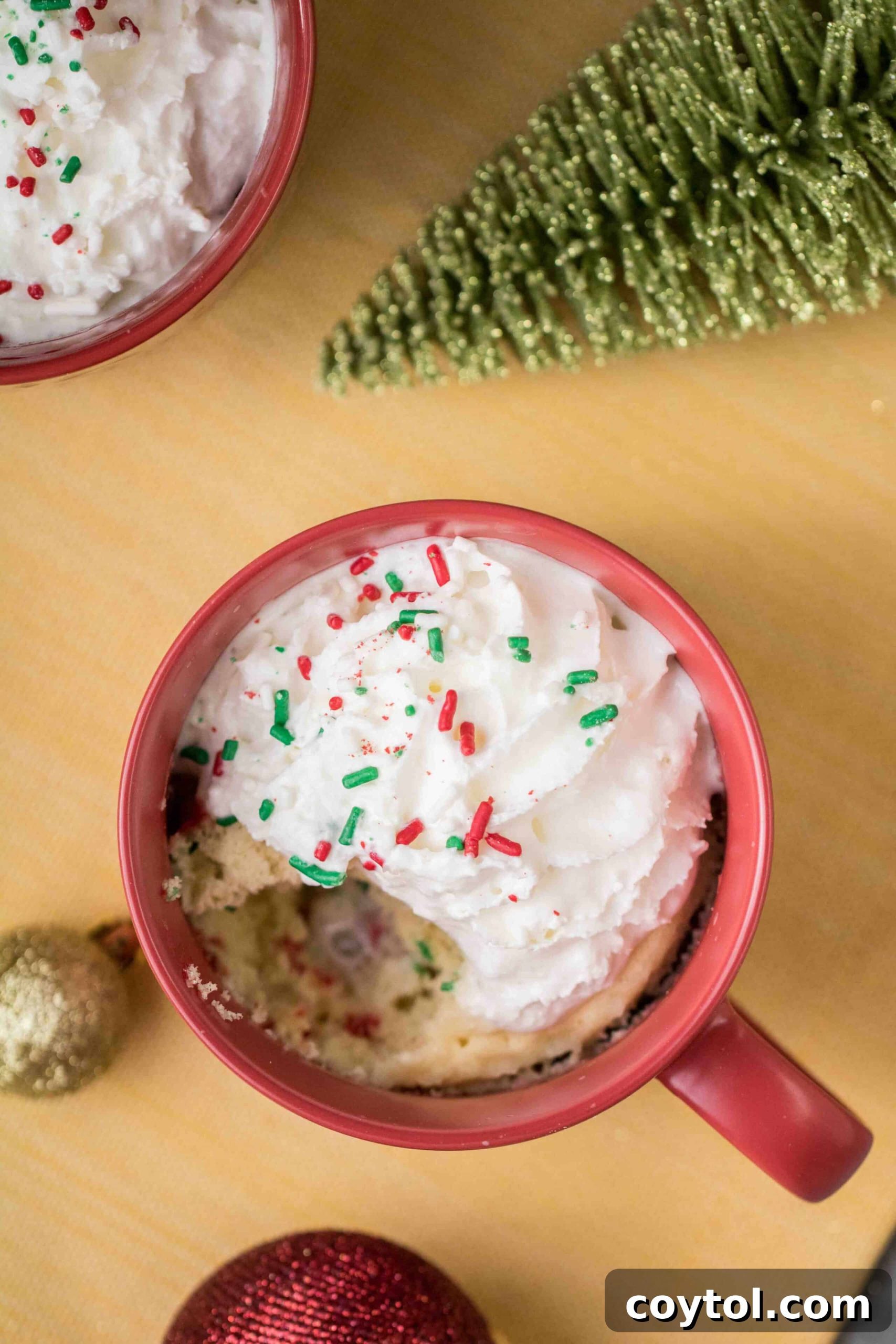 Close-up of a Christmas mug cake topped with whipped cream and sprinkles, ready to be enjoyed.