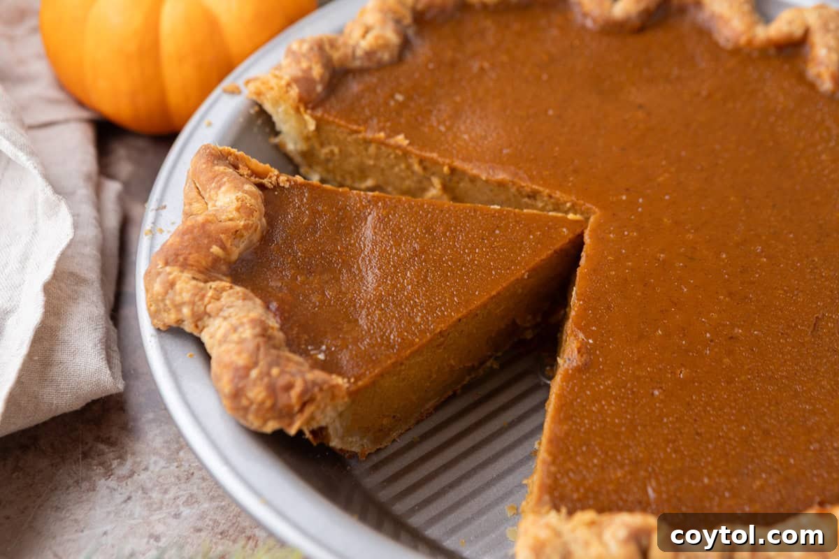 Homemade pumpkin pie with a flaky golden crust and smooth pumpkin filling with one slice cut out, showing its creamy texture.