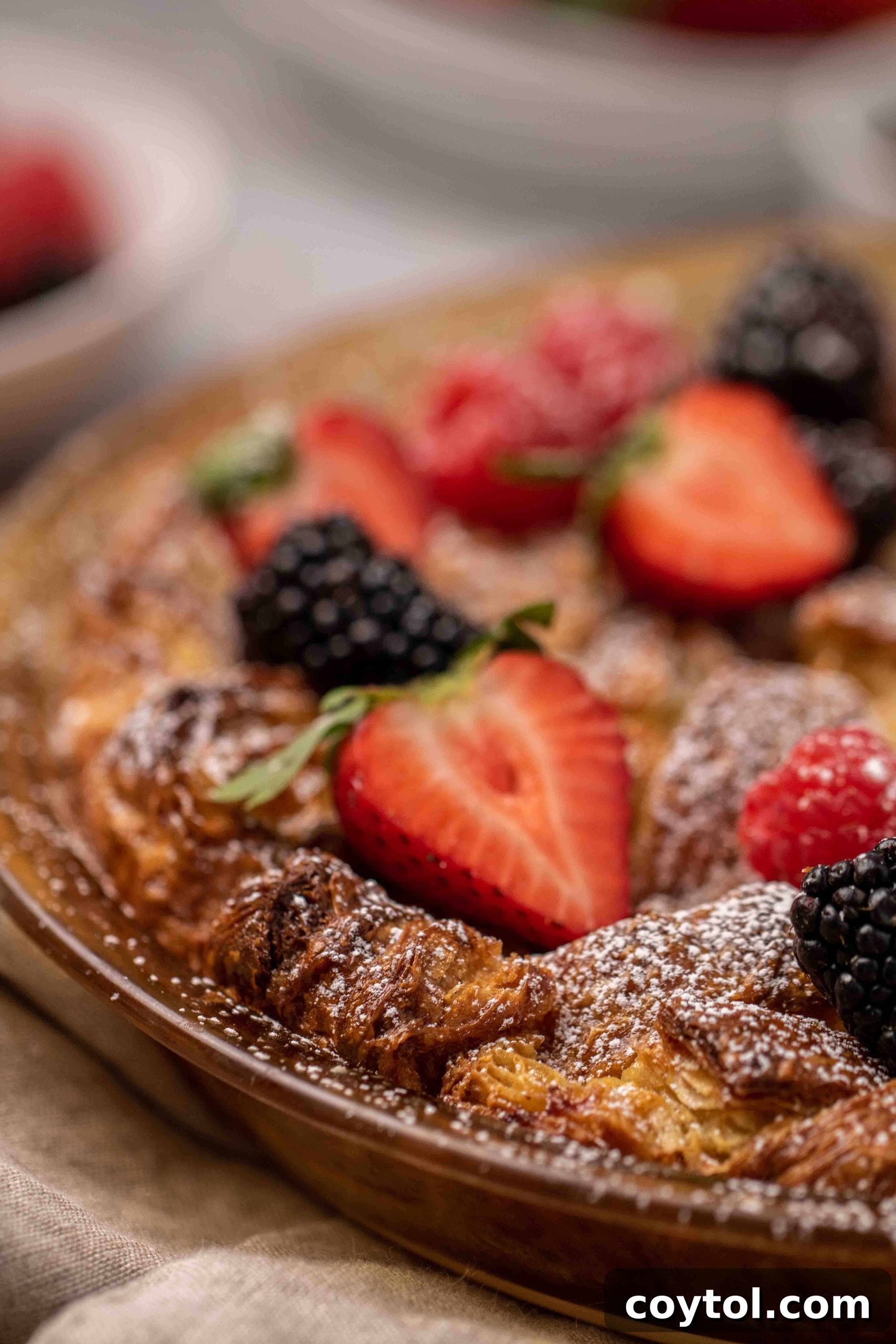 Golden Croissant French Toast Bake generously topped with fresh berries and powdered sugar