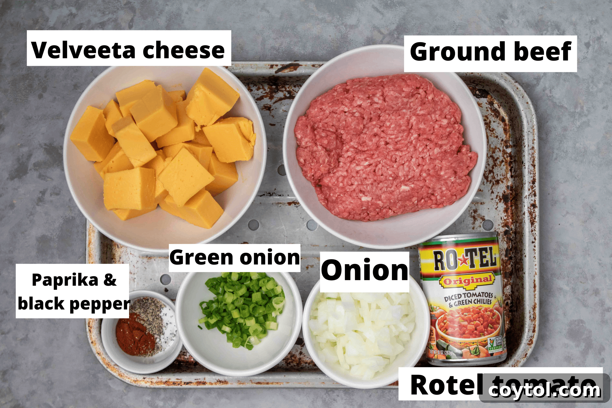 Ingredients for Rotel dip laid out on a wooden board including a block of Velveeta, a can of Rotel, ground beef, spices, and fresh vegetables.