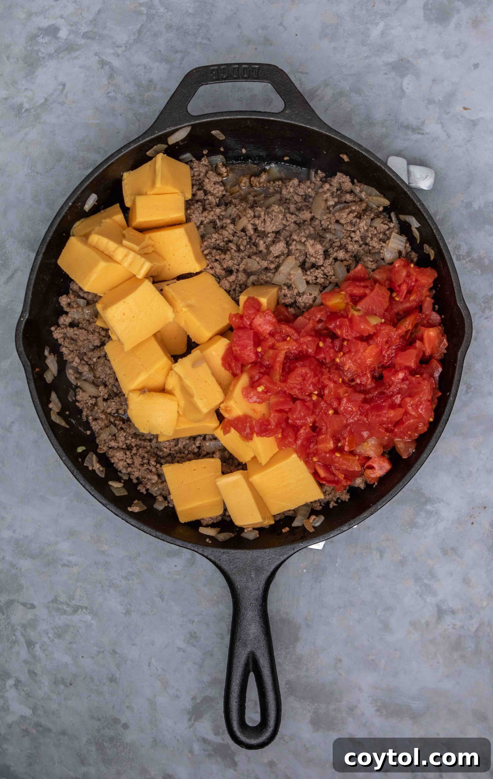 A skillet with sautéing onions and browning ground beef, seasoned with spices, as the first step in making Rotel dip.