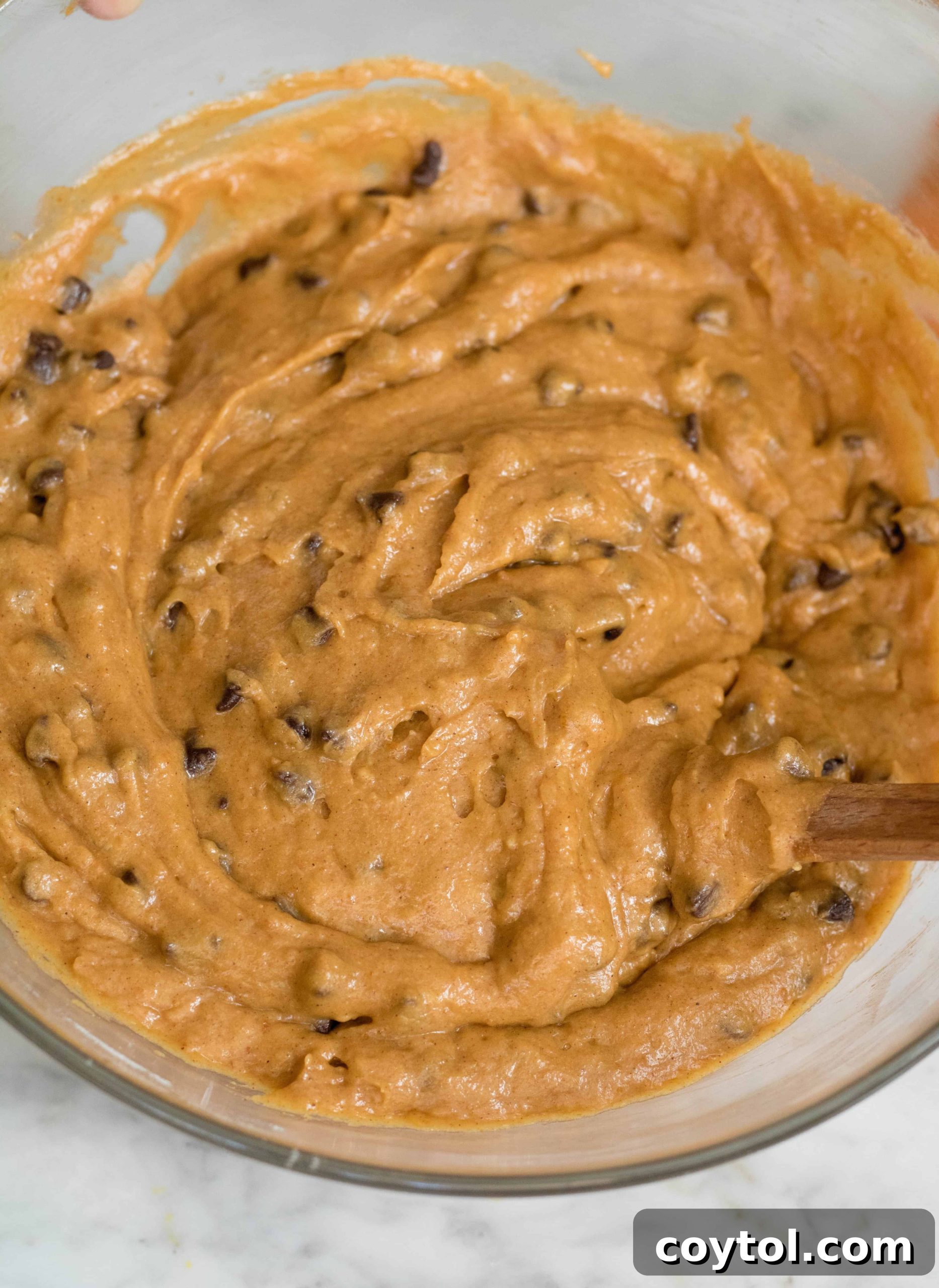 Orange-hued pumpkin muffin batter, mixed with mini chocolate chips, ready for baking.