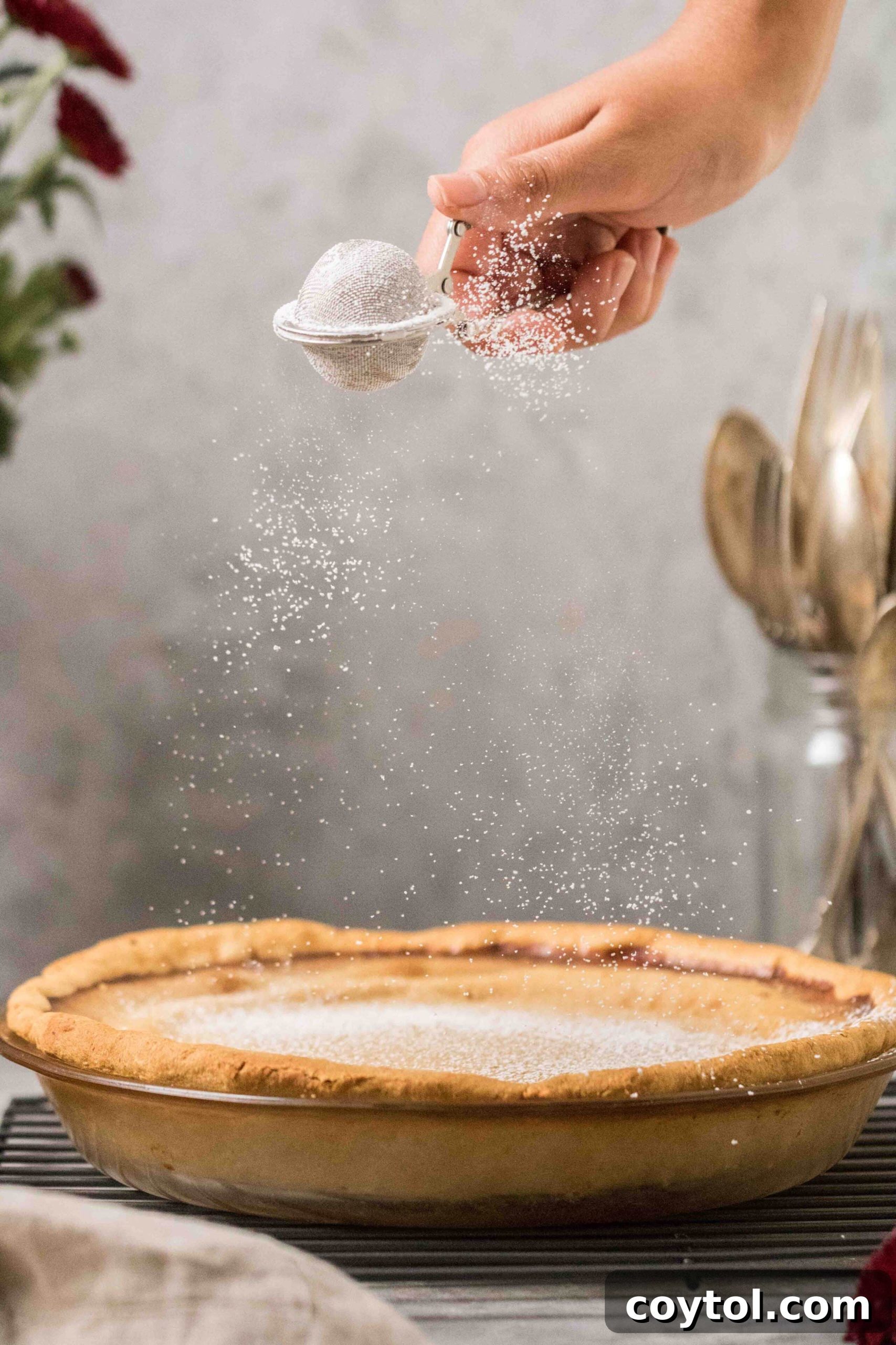 A Southern Sweet Potato Pie being dusted with powdered sugar before slicing, adding a beautiful finish.