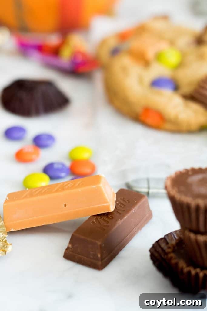 A mix of Reese's Peanut Butter Cups, KitKats, and M&M's Halloween candy on a white surface
