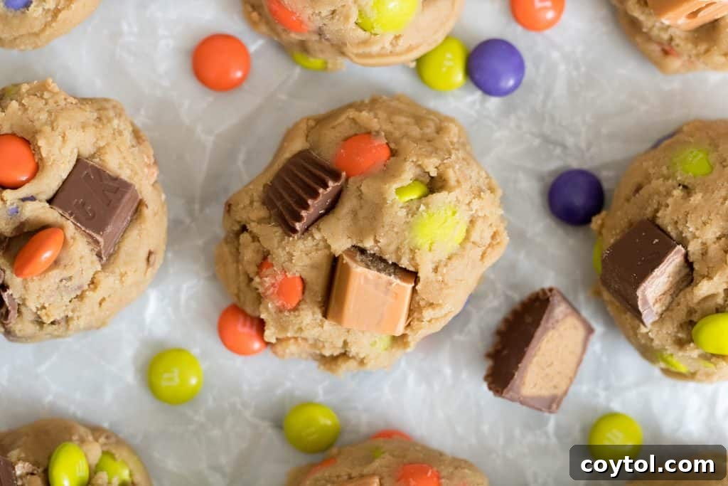 Unbaked cookie dough balls studded with colorful KitKat, Reese's, and M&M's candies on a baking sheet