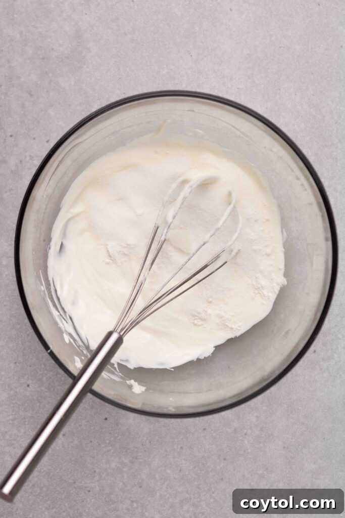 Step-by-step image 2: Adding egg, vanilla, and sugar to the cream cheese mixture for cheesecake batter.