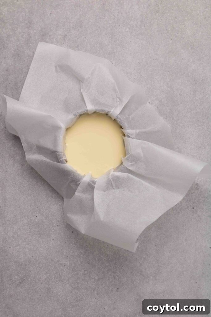 Step-by-step image 5: Pouring smooth cheesecake batter into a parchment-lined 4-inch pan.