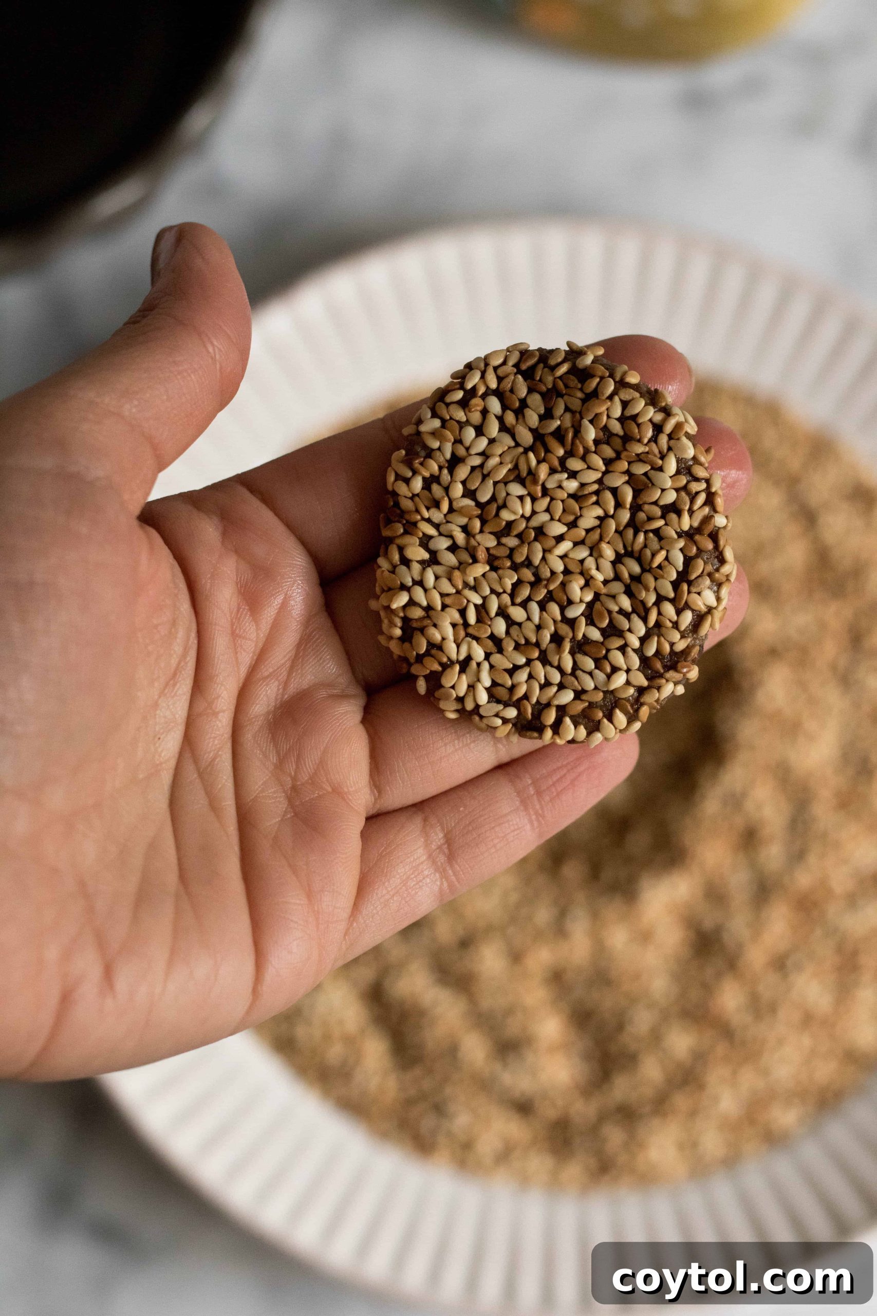 Coating a flattened tahini cookie dough ball completely with sesame seeds.