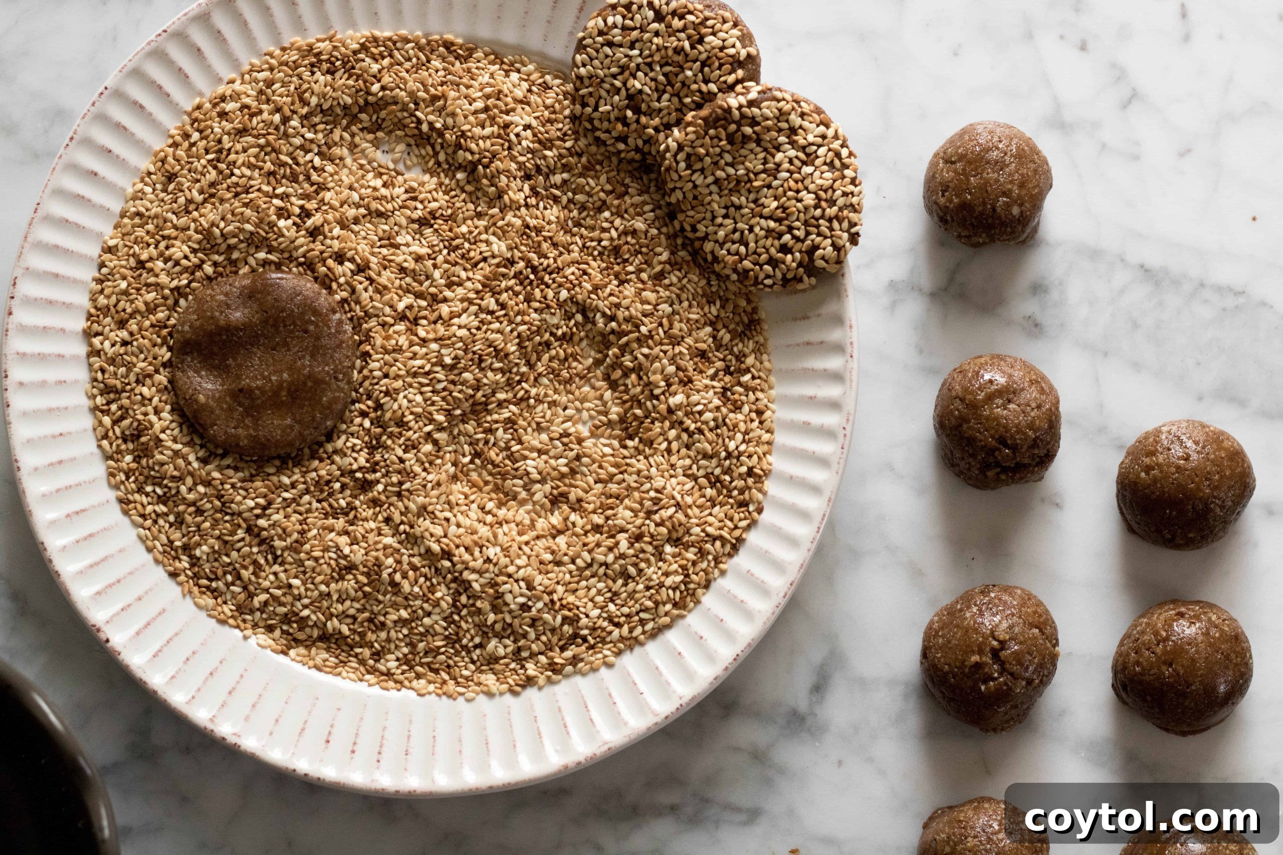 Several tahini sesame cookie dough balls being coated, showing the process.