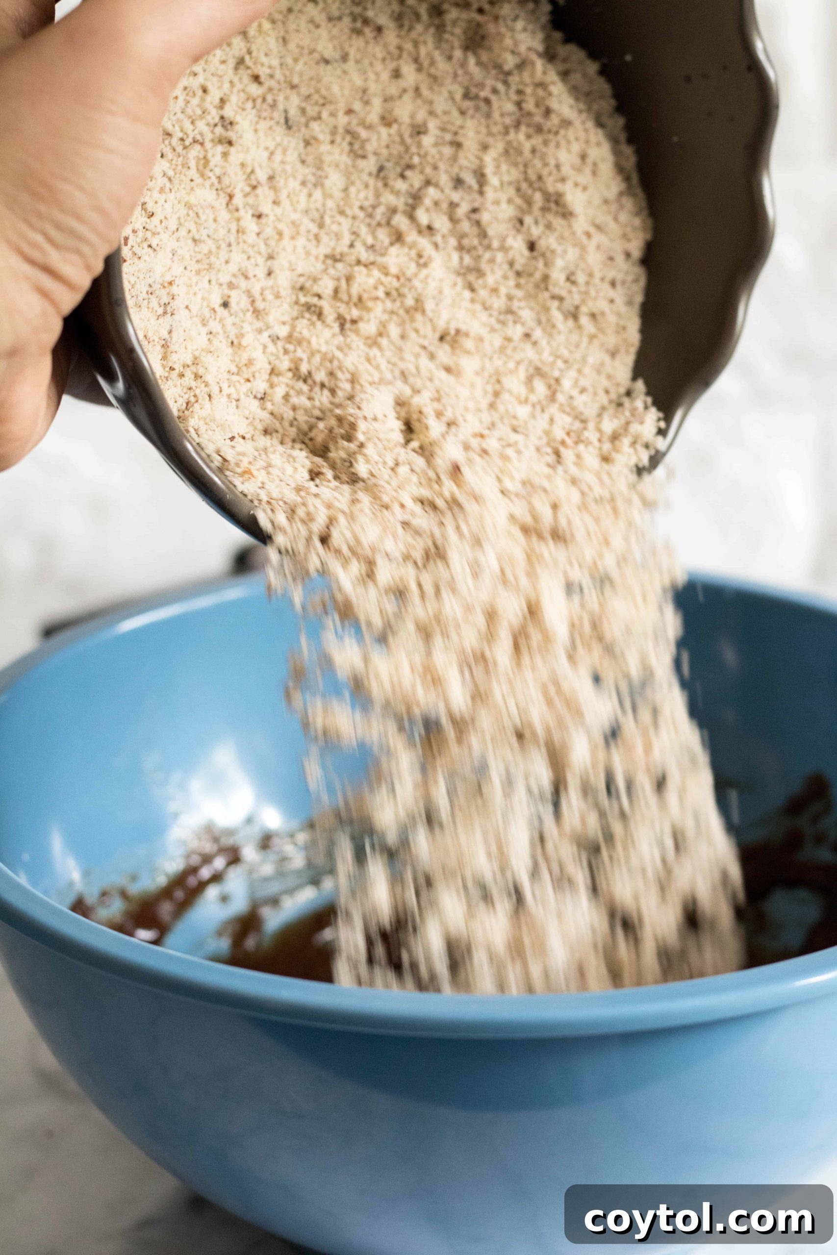 Adding almond flour to wet ingredients, forming gluten-free tahini cookie dough.