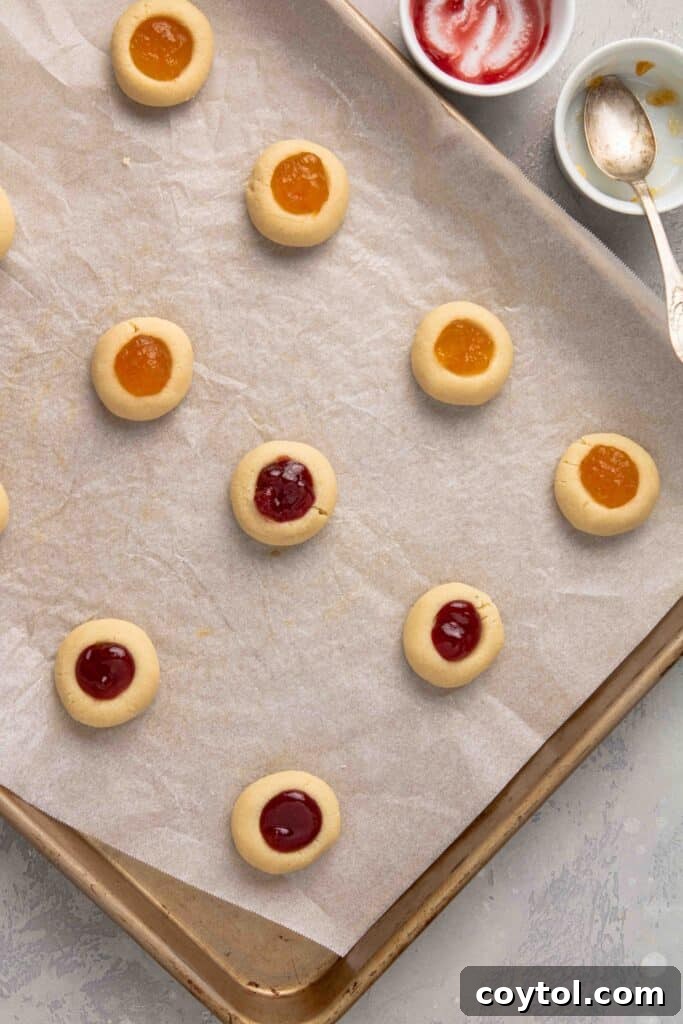 Step-by-step image: Baked jam-filled cookies cooling on a baking sheet, showing their golden edges and bubbly, set jam centers.