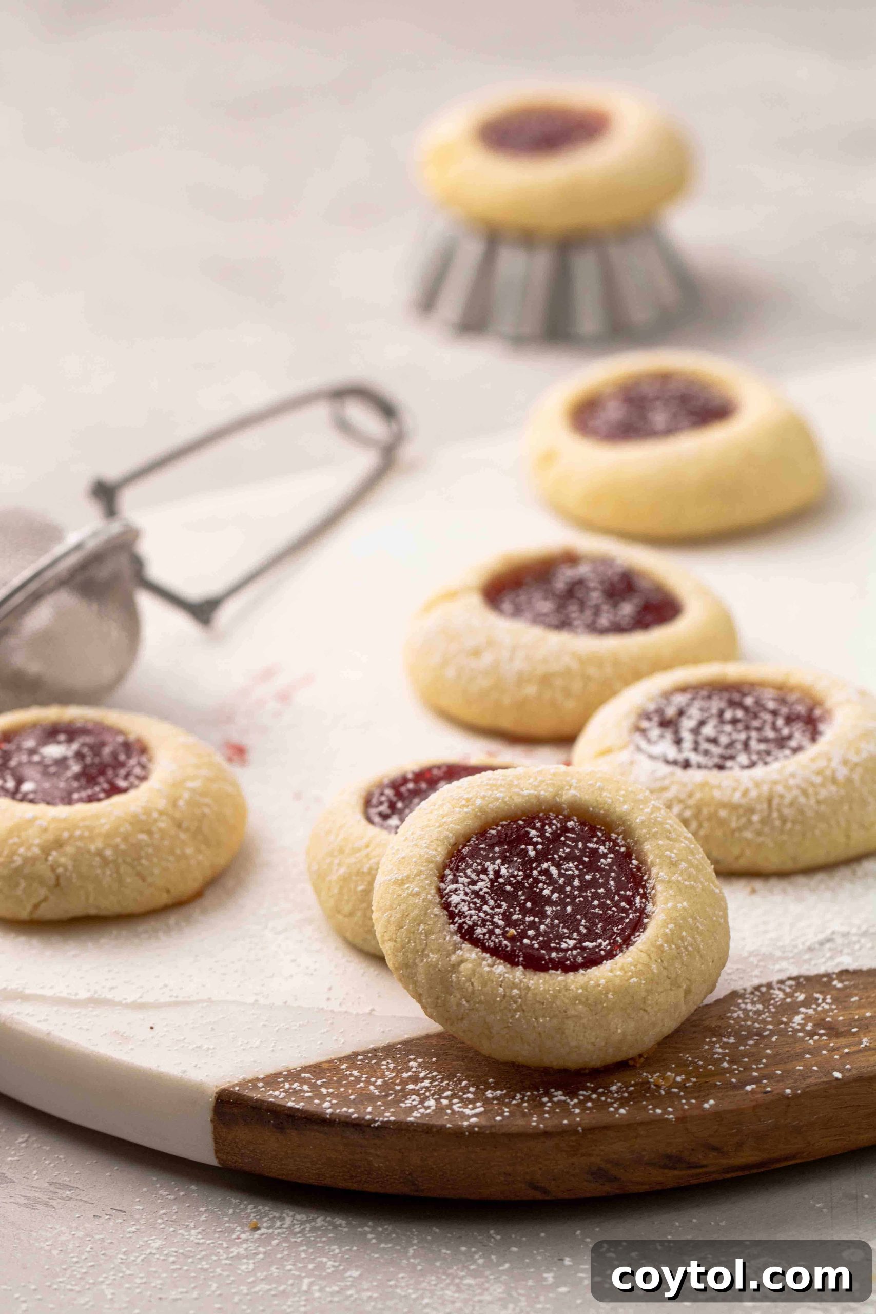 A plate piled high with various jam thumbprint cookies, some with strawberry, some with apricot, showing the variety of colors and textures.