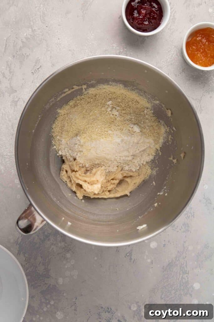 Step-by-step image: Adding dry ingredients (flour, almond flour, salt) to the creamed butter mixture in a stand mixer.