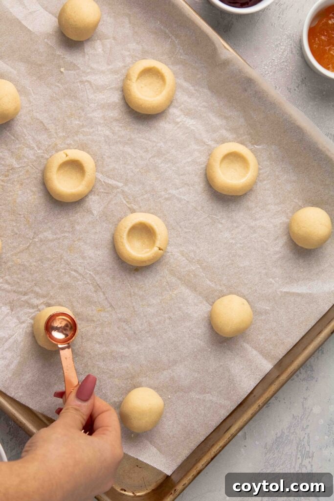 Step-by-step image: Shaping the cookie dough balls and making the thumbprint indentations on a parchment-lined baking sheet.