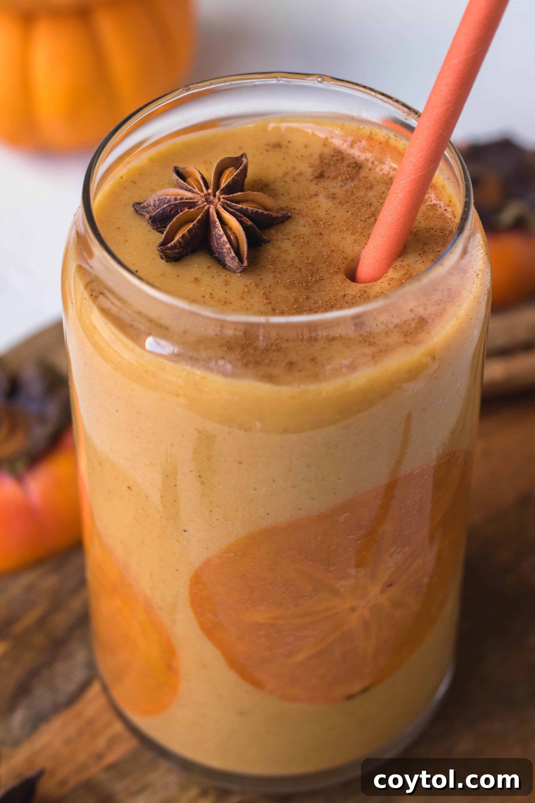 Healthy persimmon smoothie in a tall glass with a persimmon slice garnish. The glass is held against a rustic backdrop, evoking cozy autumn vibes.