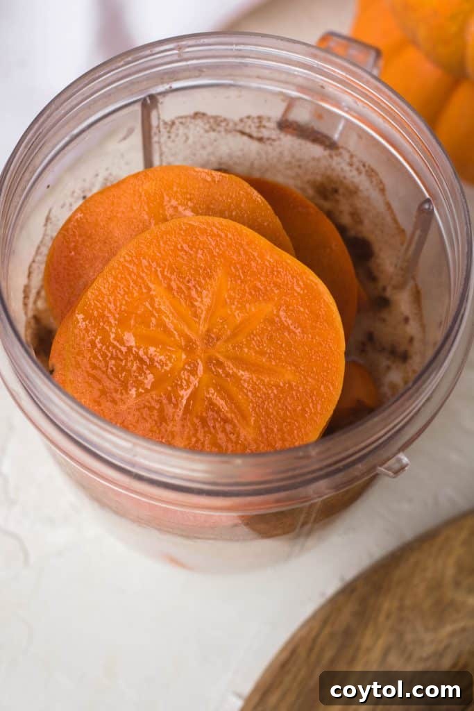 All smoothie ingredients, including freshly sliced persimmons, a splash of almond milk, and chunks of frozen banana, neatly placed in a blender cup, ready for processing.