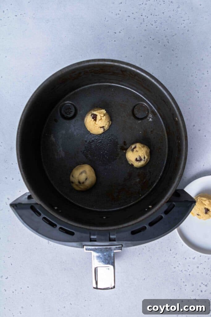 Balls of raw chocolate chip cookie dough carefully placed in an air fryer basket, ready for baking.