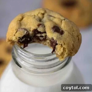 A close-up of a warm, air-fried chocolate chip cookie placed enticingly on top of a classic glass milk bottle.