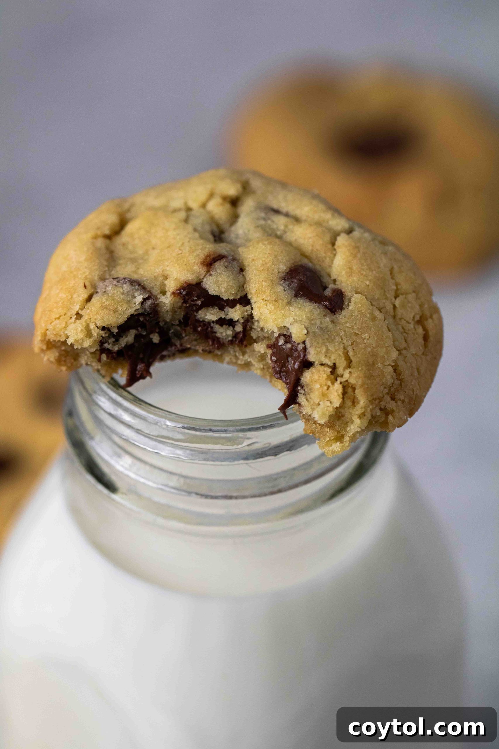 A close-up of a warm, air-fried chocolate chip cookie placed enticingly on top of a classic glass milk bottle.