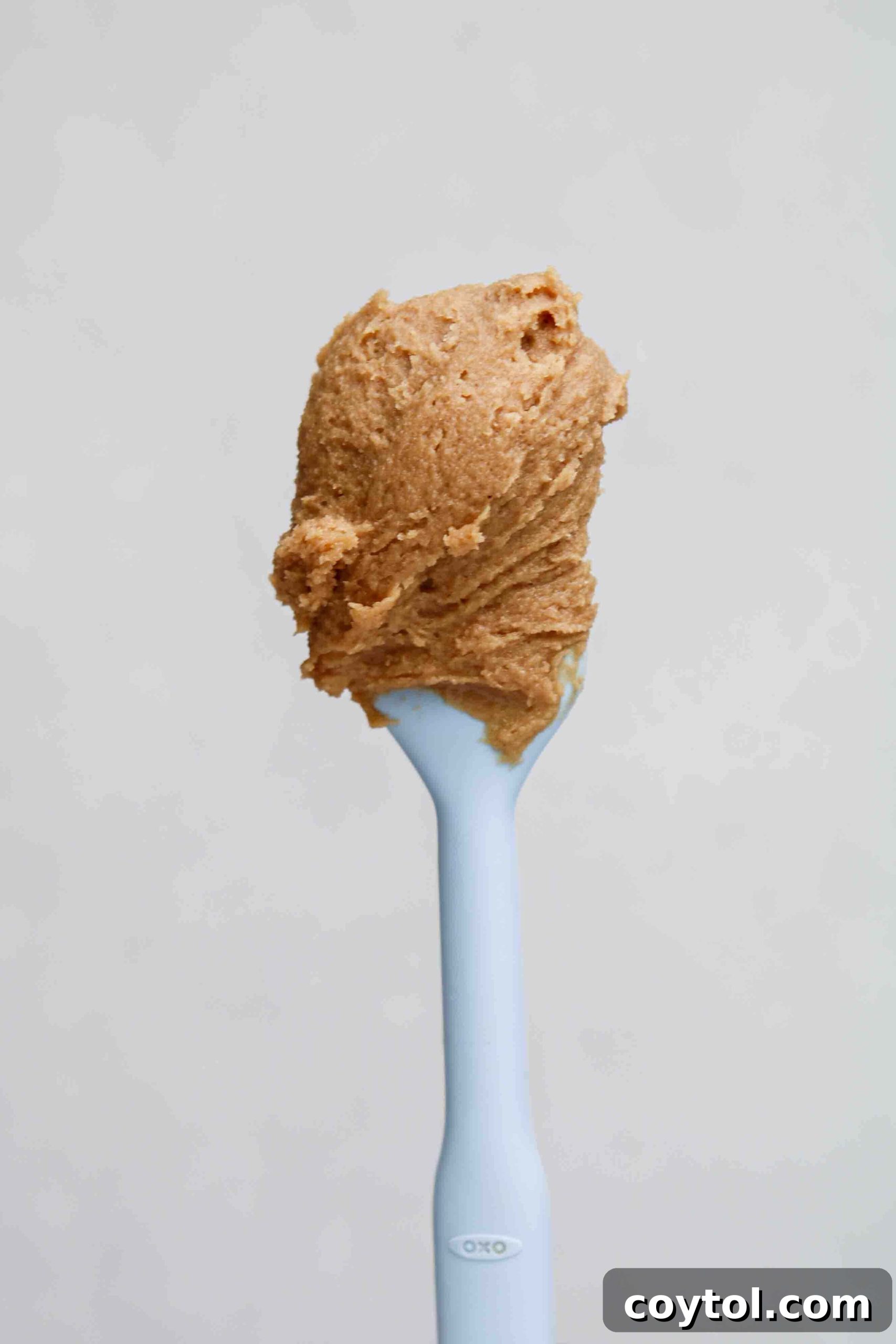 A spatula scooping soft, uniform 3 ingredient peanut butter cookie dough from a mixing bowl, ready for baking.