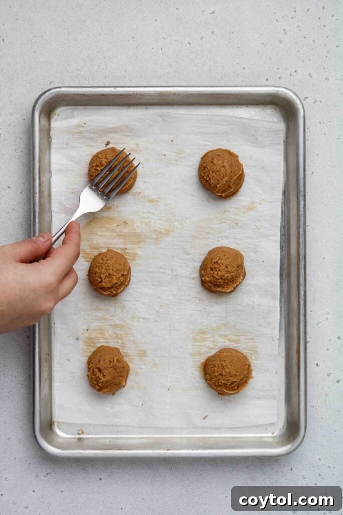 A hand gently pressing a fork onto raw peanut butter cookie dough to create the signature criss-cross pattern.