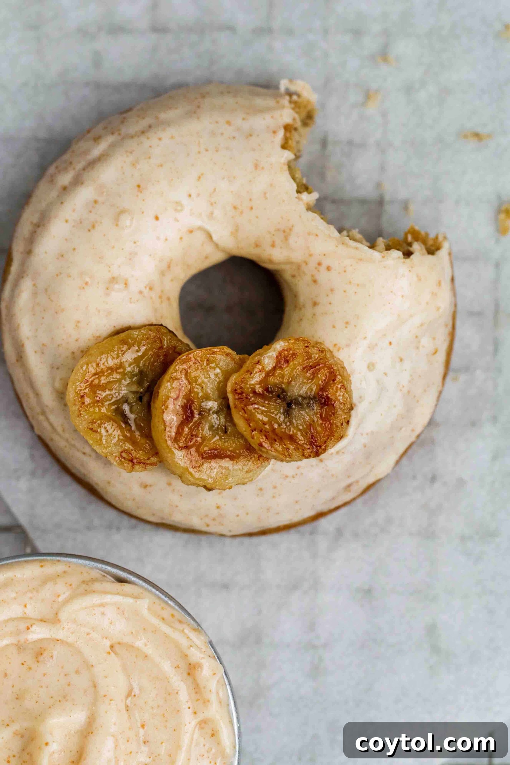 Overhead shot of a banana donut with a bite taken out, showing the glaze and moist interior.