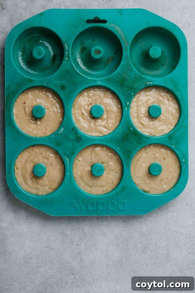 Freshly baked banana donuts cooling in a large donut pan.