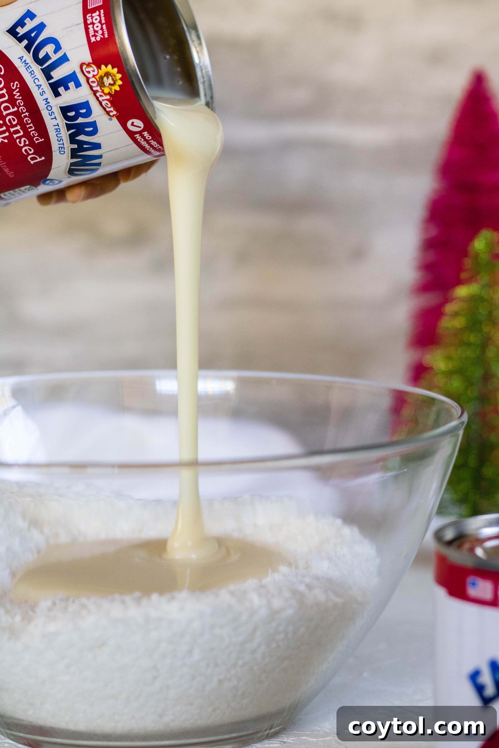 Pouring sweetened condensed milk into coconut flakes for no-bake coconut balls.