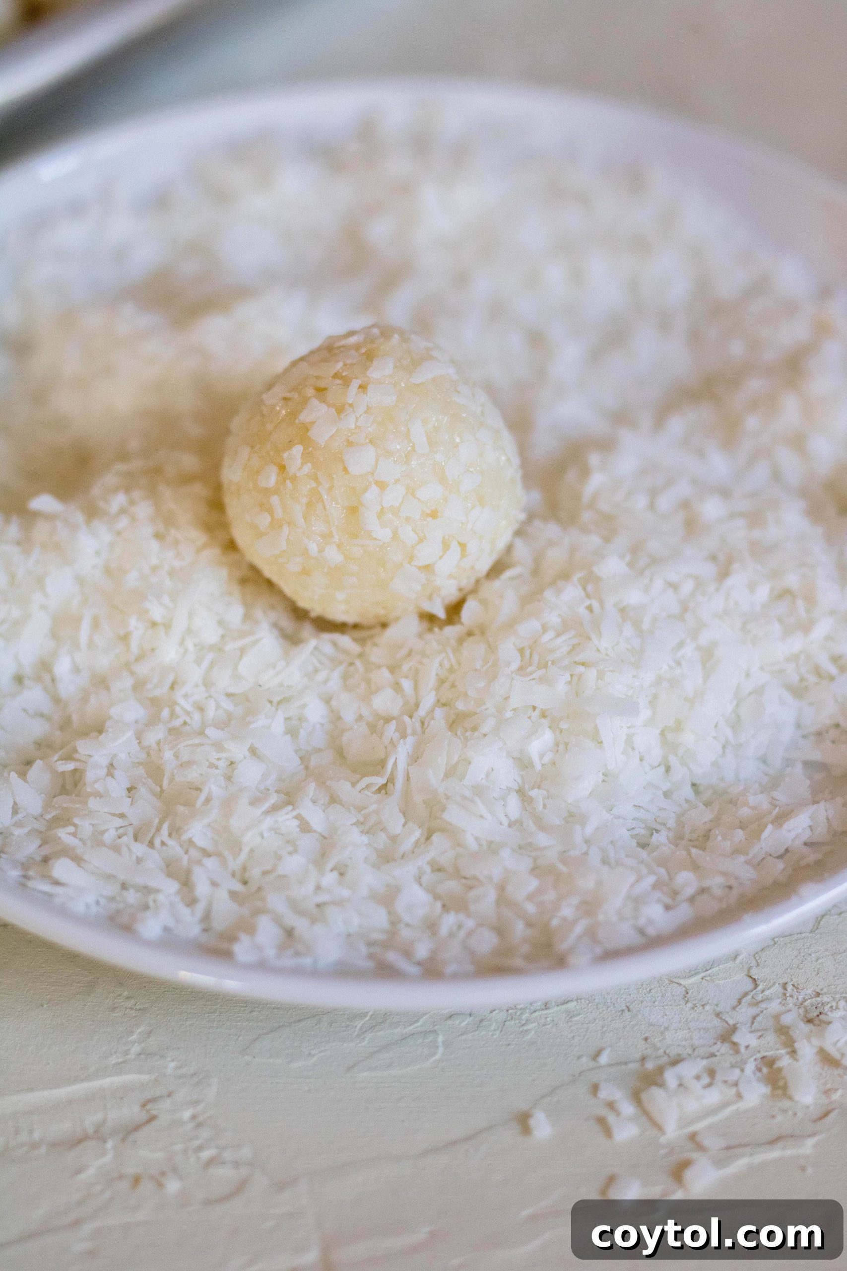 Coating the freshly rolled coconut balls with extra shredded coconut for a snowy finish.