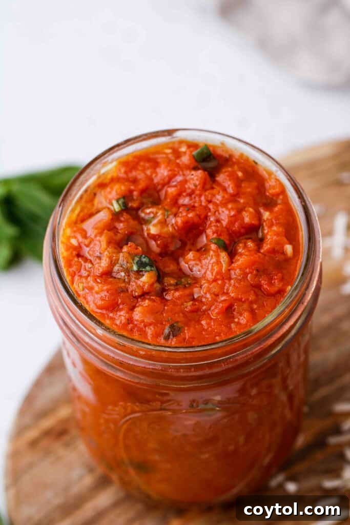 Speedy Homemade Marinara in 30 Minutes 3 Jar of homemade marinara sauce with fresh basil garnish on a rustic wooden table.
