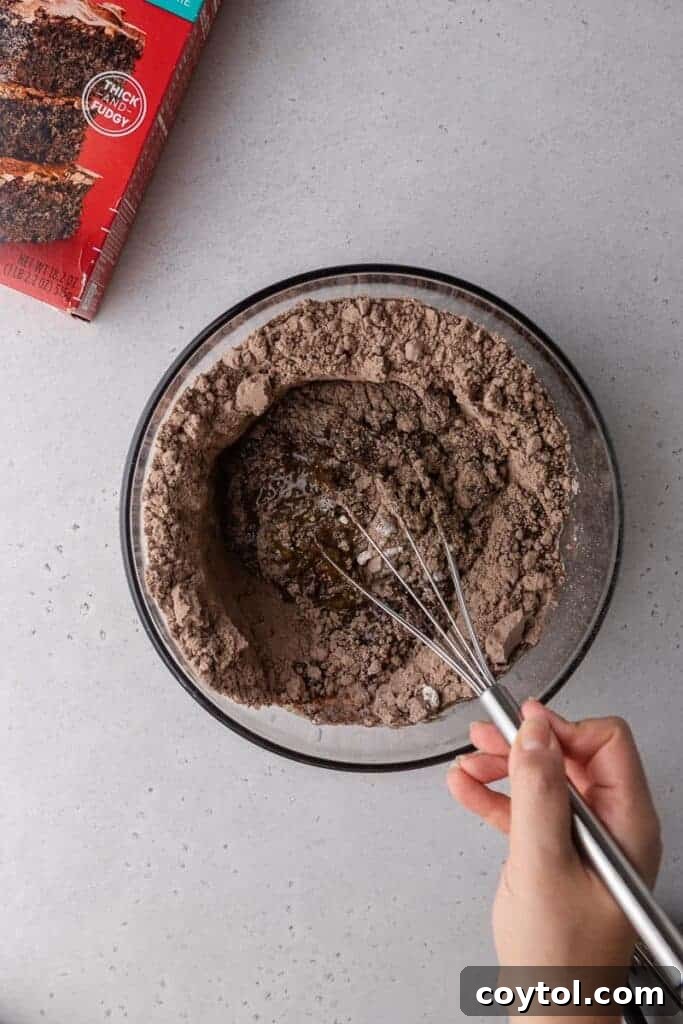 Decadent Crumbl Brownie Batter Cookies 7 A hand mixing the brownie batter cookie dough in a bowl.