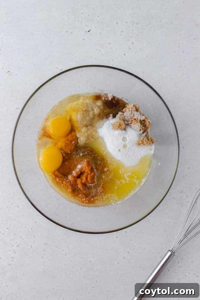Mixing bowl with wet ingredients (melted butter, mashed banana, pumpkin puree, sugars, eggs, vanilla) being whisked together for pumpkin banana bread.