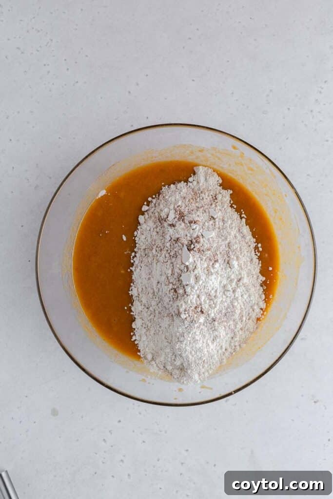 Dry ingredients (flour, baking soda, salt, spices) being added to the wet mixture in a large bowl.
