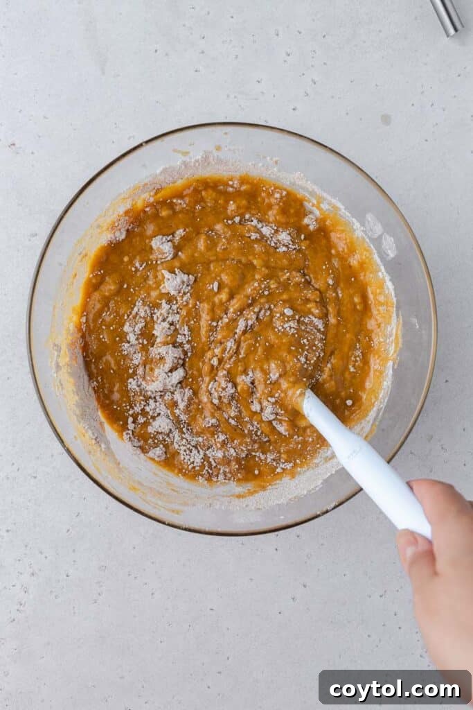 Batter forming as wet and dry ingredients are gently combined in a mixing bowl for pumpkin banana bread.