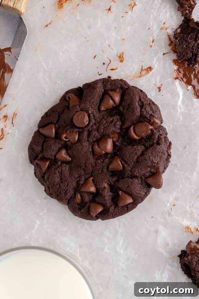 Thick Dark Dream Double Chocolate Cookies 3 A single Crumbl Dark Dream chocolate cookie on parchment paper, adorned with extra semi-sweet chocolate chips for a rich, appealing look.