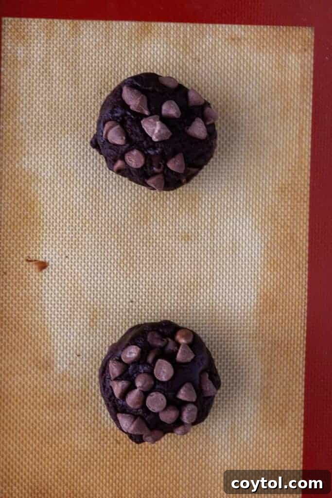 Thick Dark Dream Double Chocolate Cookies 7 Perfectly scooped double chocolate cookie dough balls, generously topped with extra chocolate chips, arranged on a silicone baking mat ready for the oven.